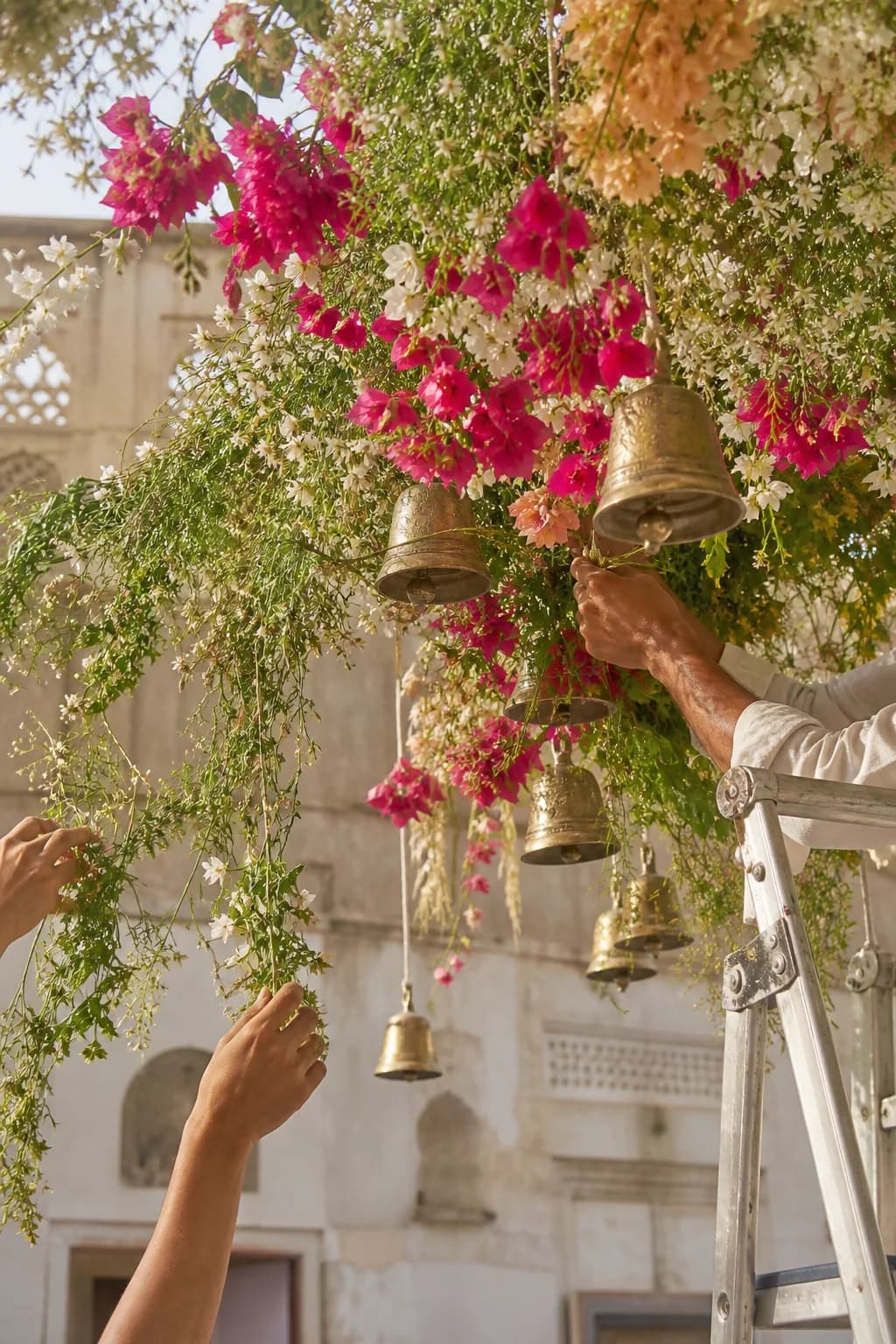 Floral designers weaving jasmine and brass bells into an installation